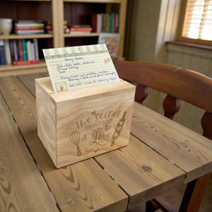 Wooden box with a card on a wooden table in a room with books and a chair.
