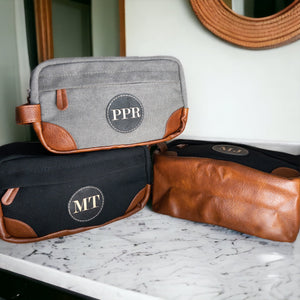 Close-up of a hanging Dopp Kit’s leather patch, hinting at the customization option. Bag’s canvas material evident in the backdrop.