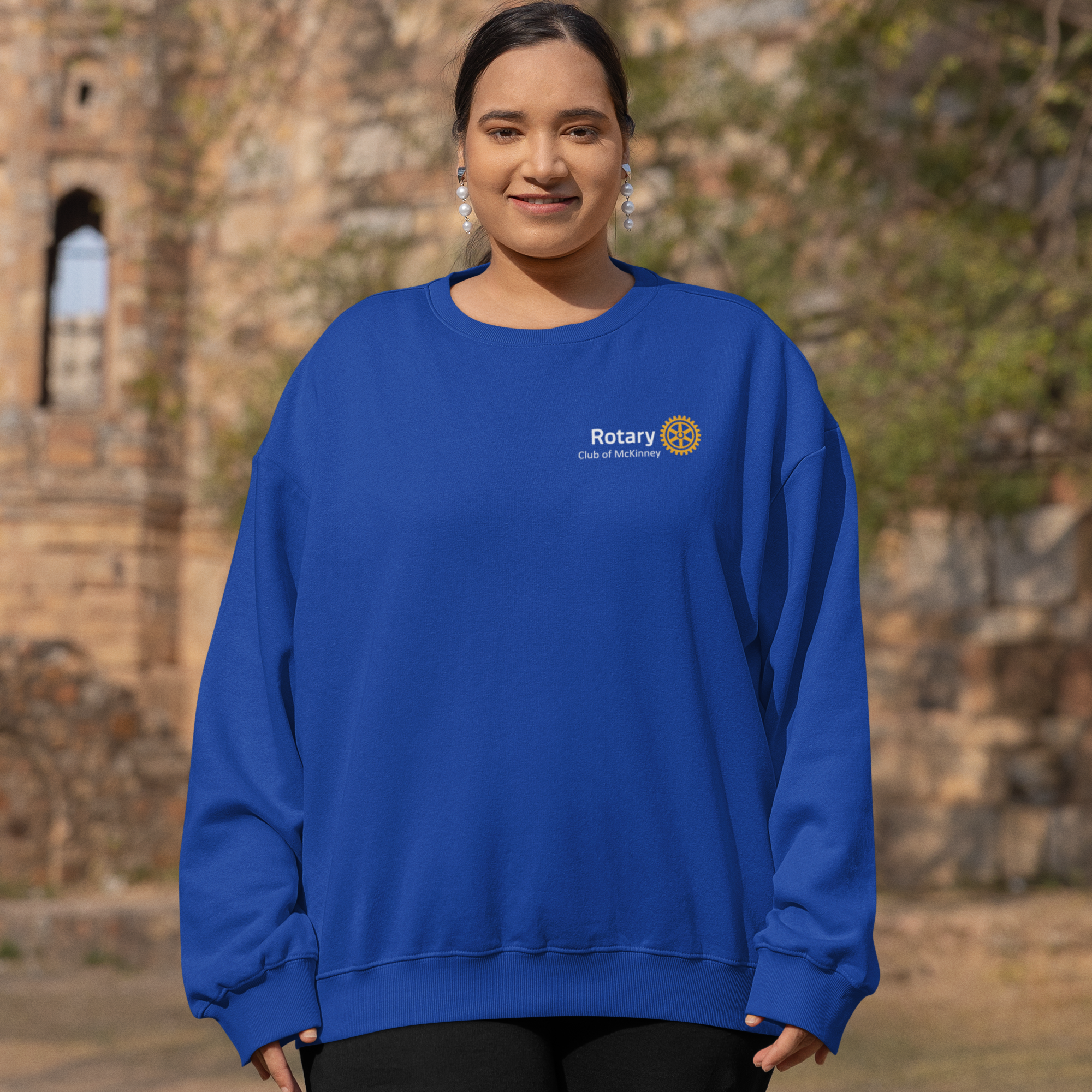 Person wearing a blue sweatshirt with a Rotary logo in front of stone ruins.
